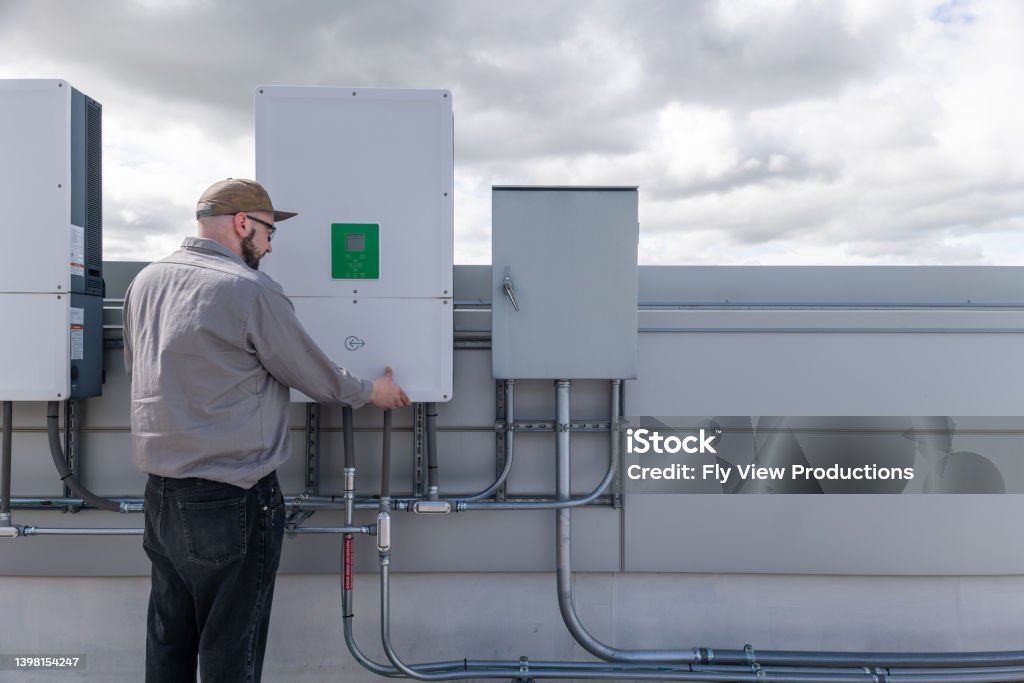 A professional worker does maintenance on a solar panel control board while servicing an energy efficient smart home outfitted with solar panels.